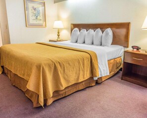 Una habitación de hotel con una cama grande, cabecero de madera, dos lámparas de noche, una mesita y un cuadro en la pared.