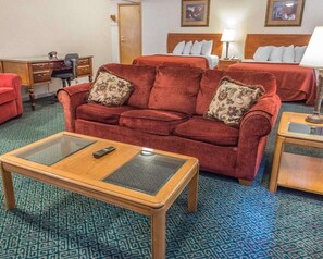 Habitación de hotel con un sofá rojo, una mesa de centro de madera, un escritorio con una silla y dos camas con ropa de cama roja.