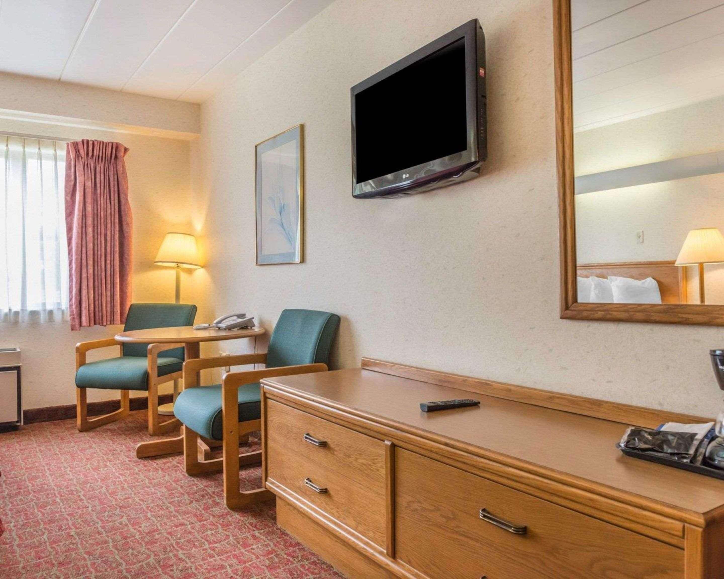 Ein Hotelzimmer mit einem Holztisch, zwei Stühlen, einem Fernseher, einem Spiegel, einer Lampe und einem Telefon.