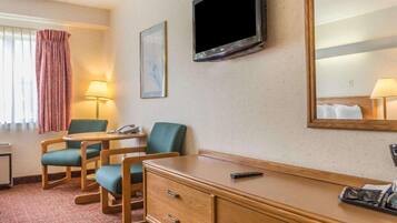 Ein Hotelzimmer mit einem Holztisch, zwei Stühlen, einem Fernseher, einem Spiegel, einer Lampe und einem Telefon.