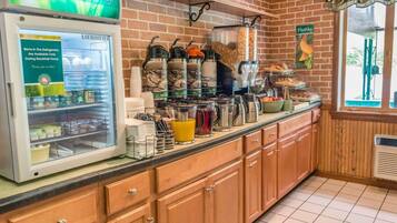 A breakfast bar with a refrigerator displaying items available during breakfast hours, a coffee station with multiple coffee makers, and a window with a view of the outdoors.