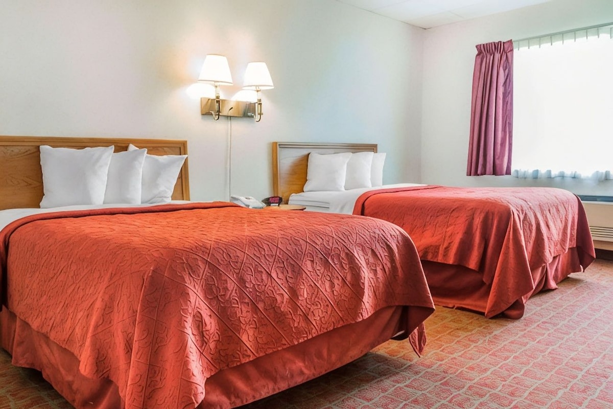 A hotel room with two beds, a patterned carpet, and a window with curtains.