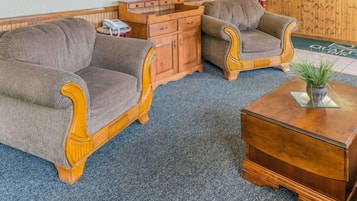 Un hall d’hôtel avec deux fauteuils rembourrés, une table basse en bois, une petite table d’appoint avec un téléphone et un comptoir de réception.