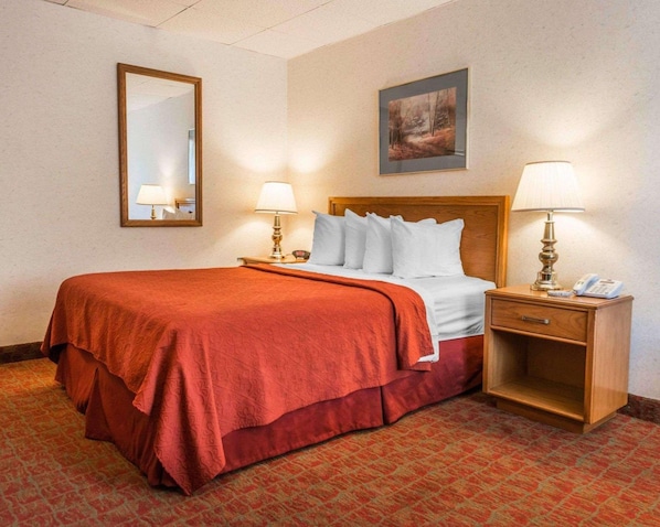 Habitación de hotel con cama, dos lámparas de noche, mesita con teléfono, espejo y un cuadro en la pared.
