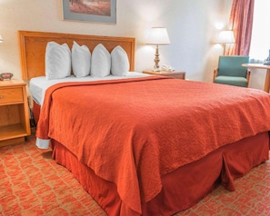 Una habitación de hotel con una cama grande, un cabecero de madera, una mesita de noche, una lámpara y una silla.