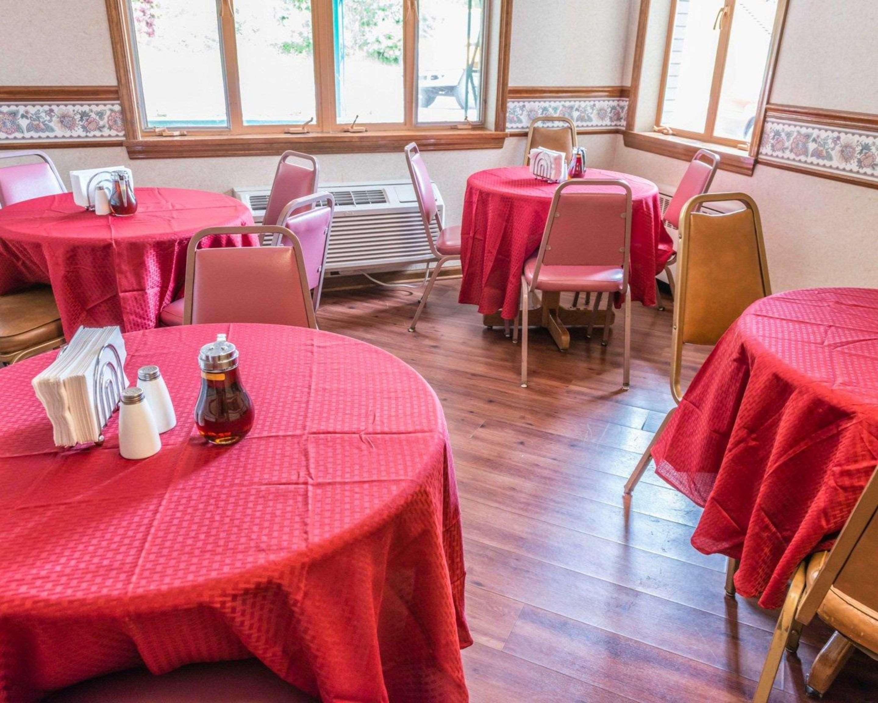 A dining area with round tables covered in red tablecloths, wooden chairs, and a central air conditioning unit.