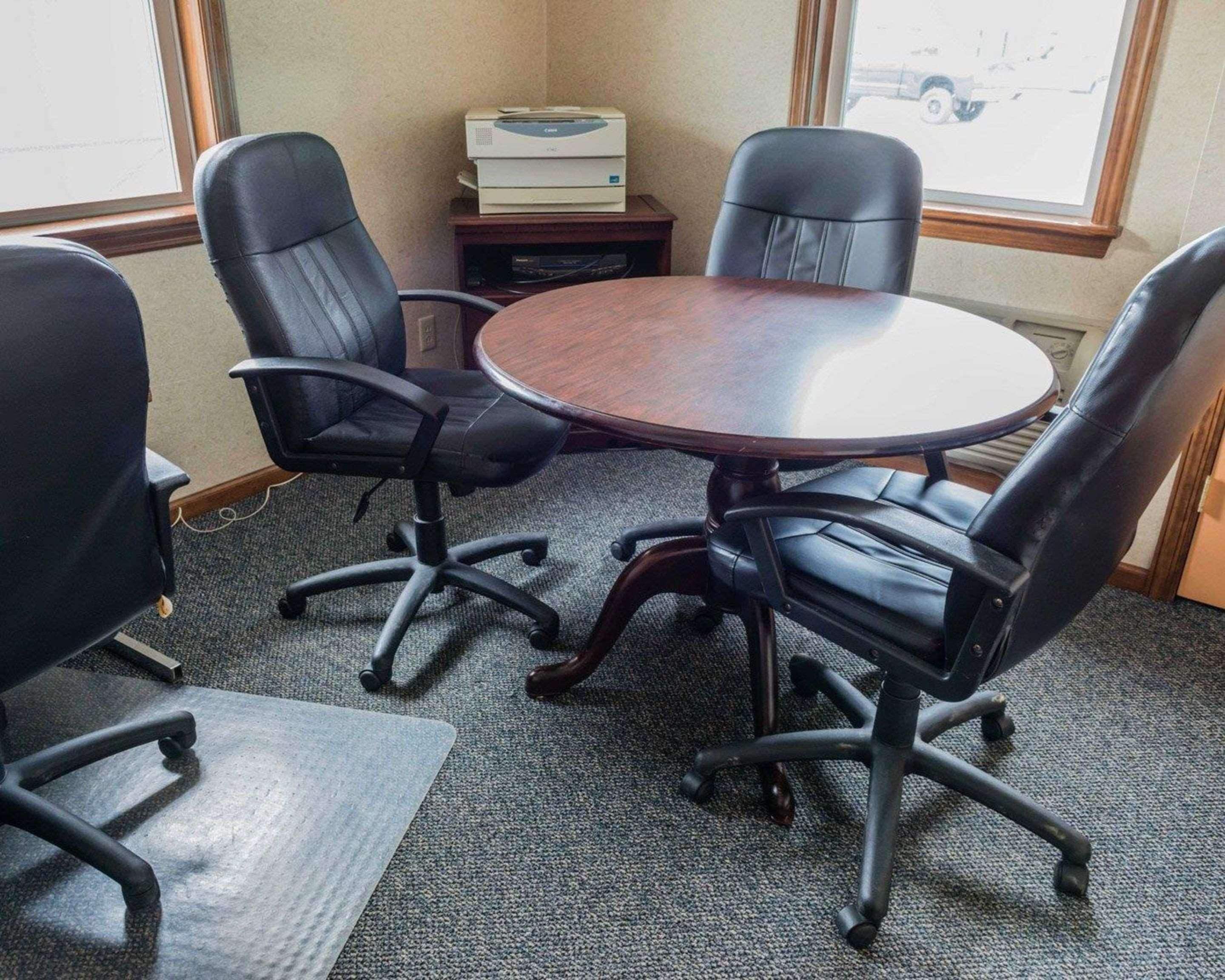 Une salle de conférence équipée d’une table ronde, de quatre chaises de bureau noires, d’une imprimante et d’une fenêtre donnant sur l’extérieur, avec vue sur un véhicule.