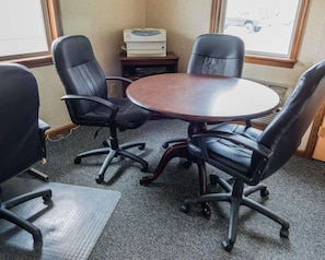 A conference room with a round table, four black office chairs, a printer, and a window with a view of a vehicle outside. - Quality Inn Royle (Kittanning)