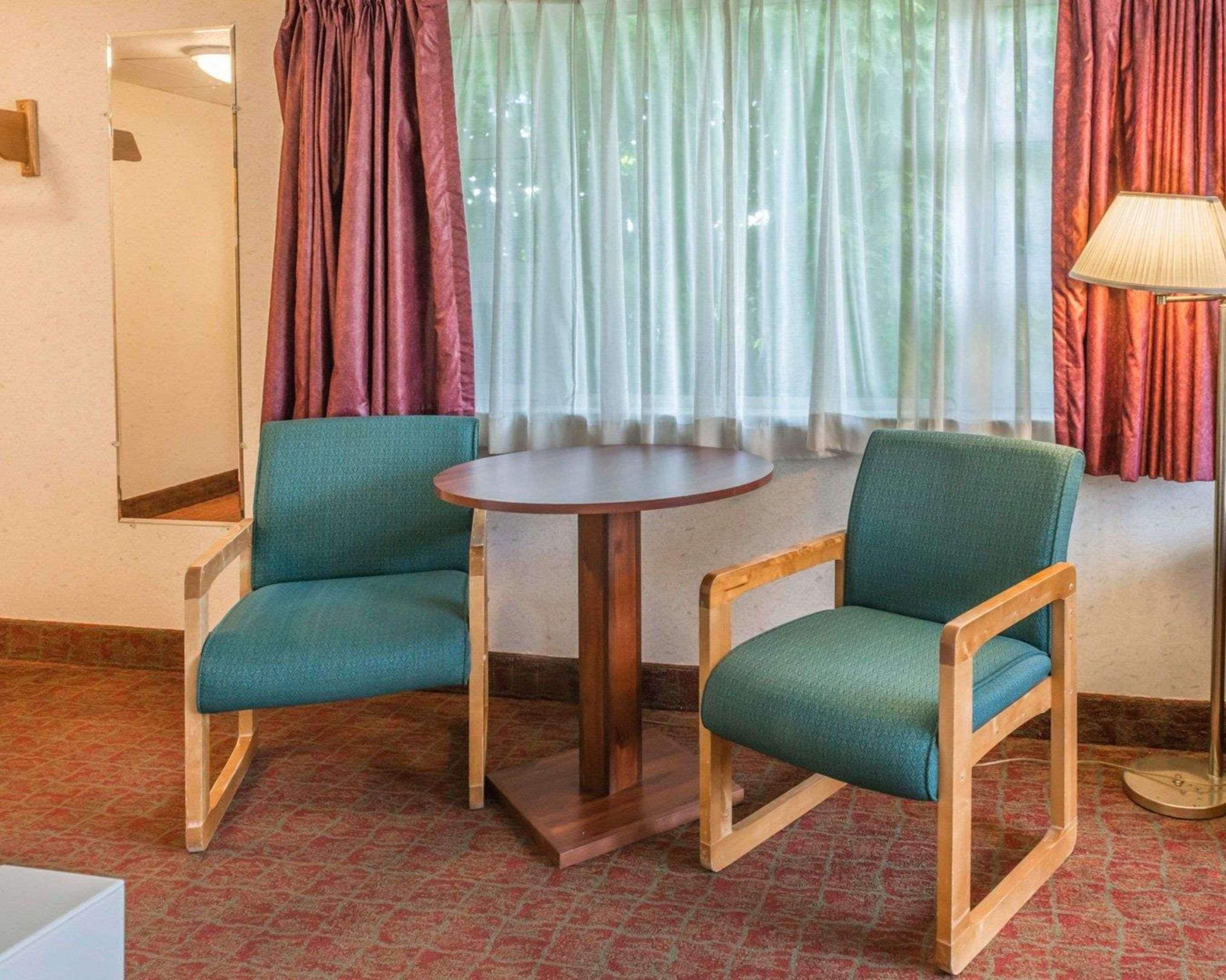 A room with two teal chairs, a round wooden table, a mirror, and a lamp.