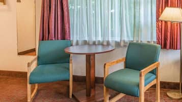 A room with two teal chairs, a round wooden table, a mirror, and a lamp.