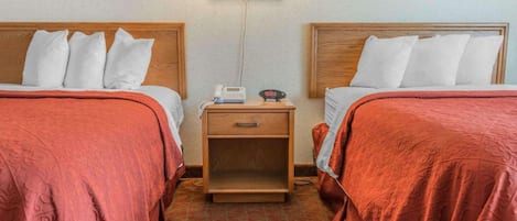 Et hotelværelse med to senge, hver med en trægavl, et natbord med telefon og vækkeur, samt en lampe fastgjort på væggen.