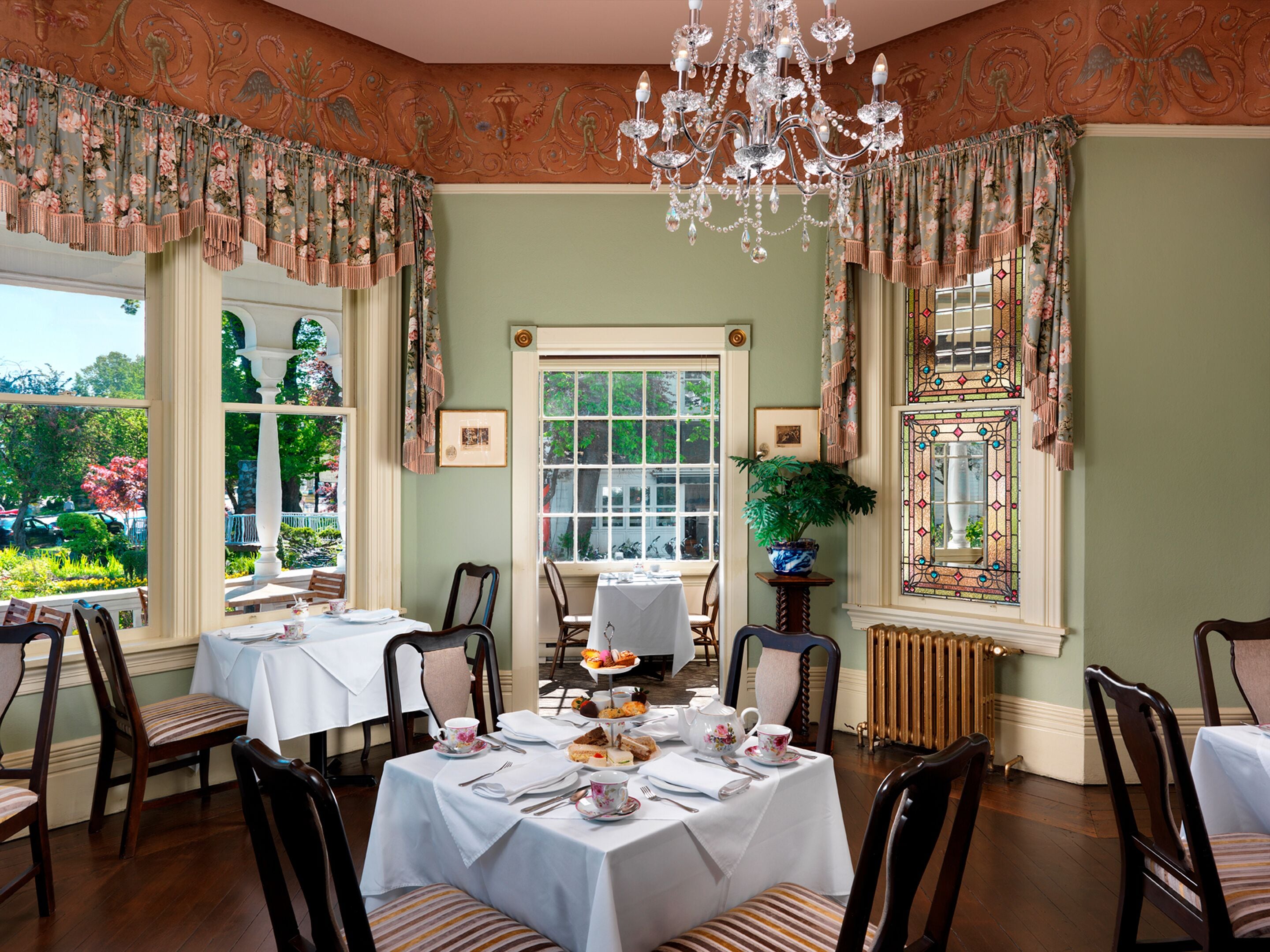 Ein Esszimmer mit einer Chandelüster, floralen Vorhängen und Blick auf den Garten.