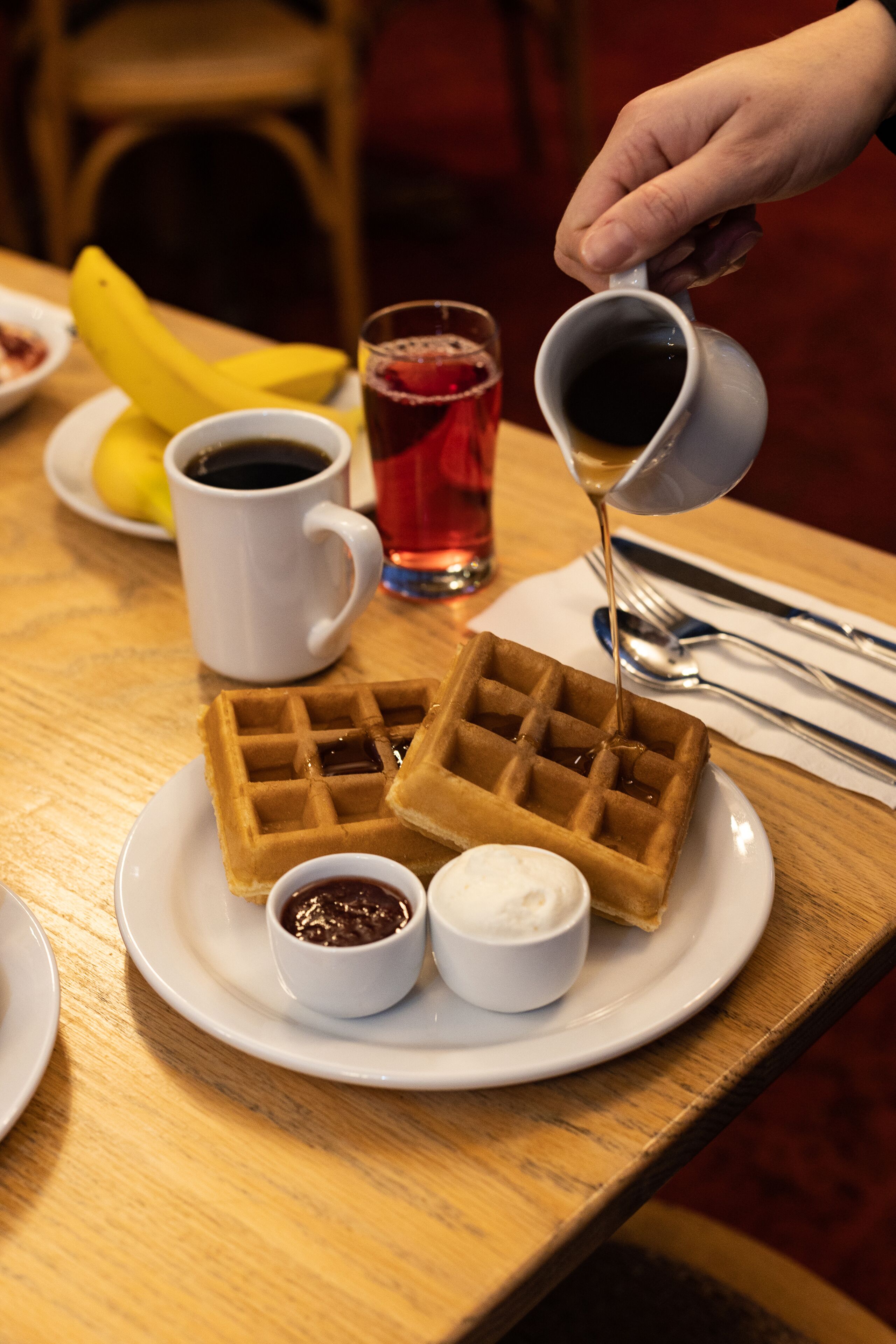 Une assiette contenant des gaufres, du sirop et deux petits bols de condiments, le tout posé sur une table en bois.