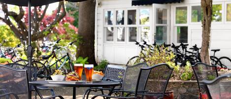 An outdoor seating area with metal chairs and a table, a black umbrella, and a white building in the background.