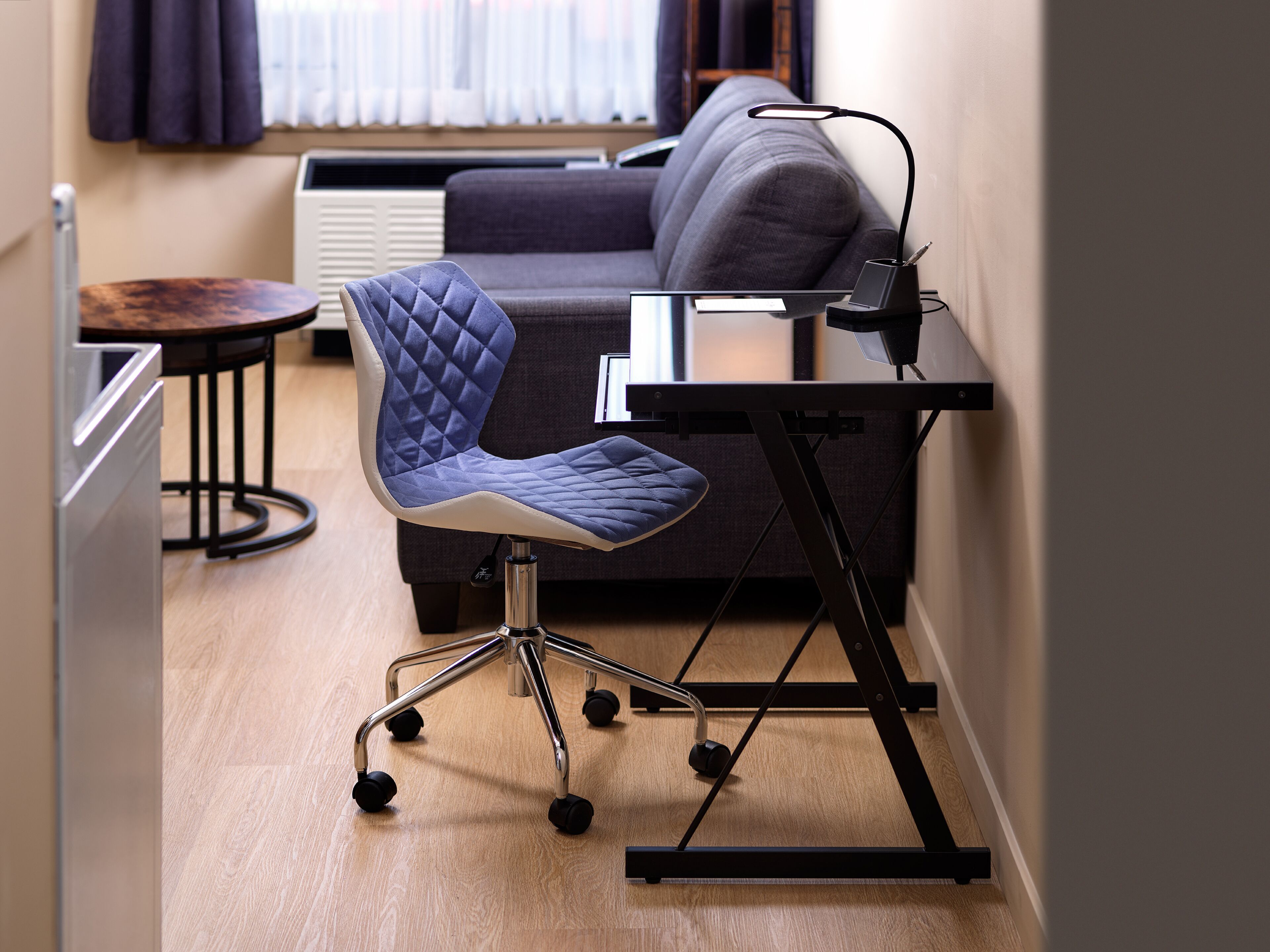 Una silla de oficina moderna con respaldo acolchado y ruedas, sobre un escritorio de metal negro con una lámpara.