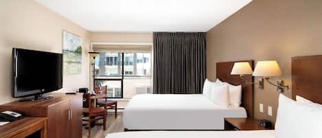 A hotel room with a flat-screen TV, a desk with a chair, two beds, a window with curtains, and a wall-mounted lamp.