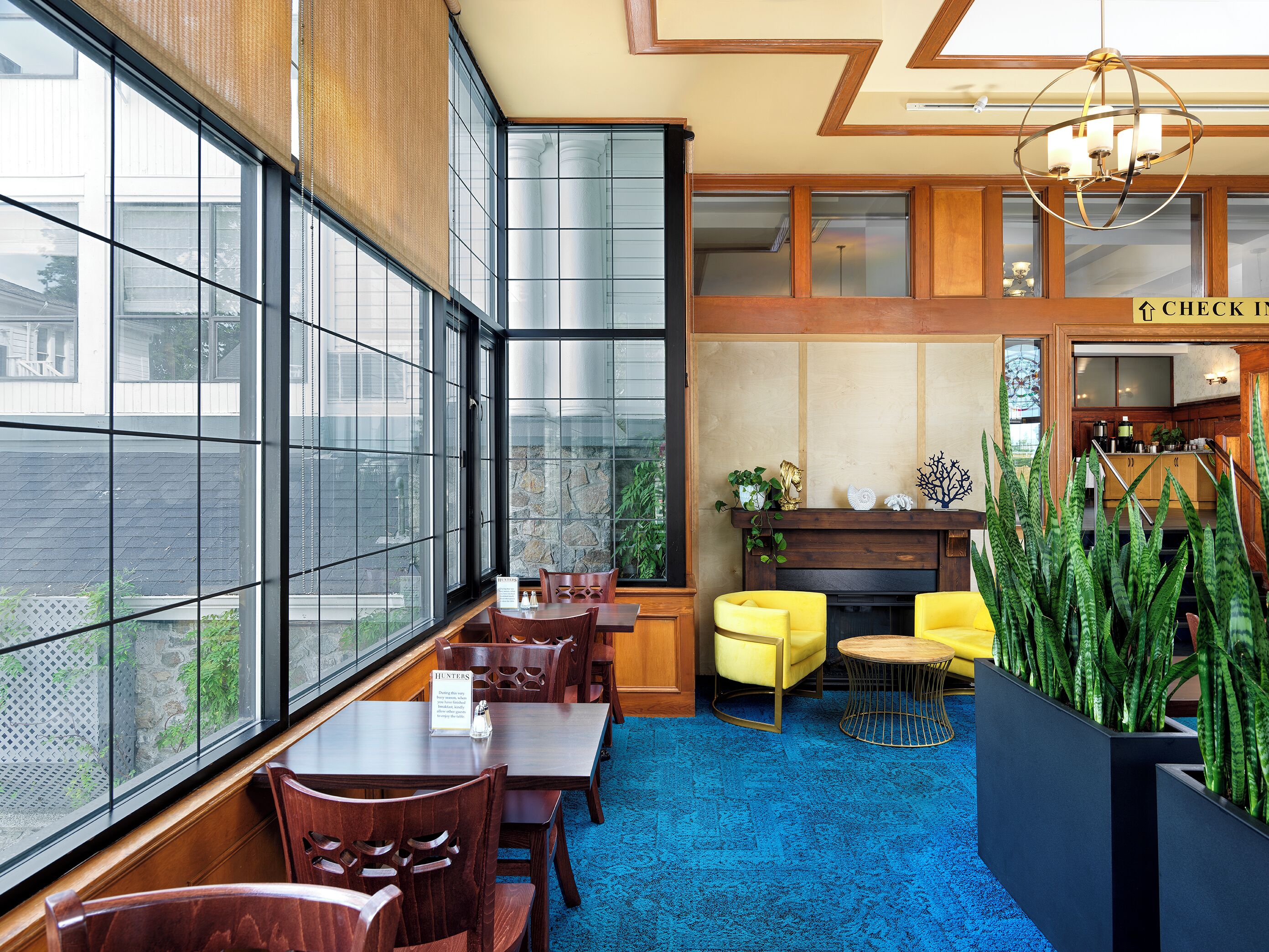 A restaurant with large windows, wooden furniture, a blue carpet, and a fireplace.
