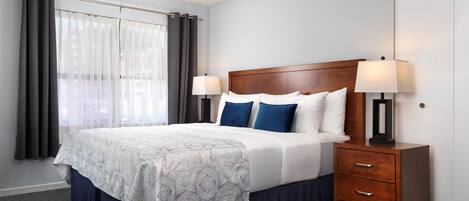 Habitación de hotel con cama, dos mesitas de noche con lámparas, cabecera de madera y ventana con cortinas.