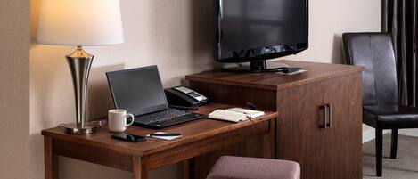Hotelkamer met een houten bureau, een laptop, een televisie, een telefoon, een lamp, een stoel en een klein krukje.