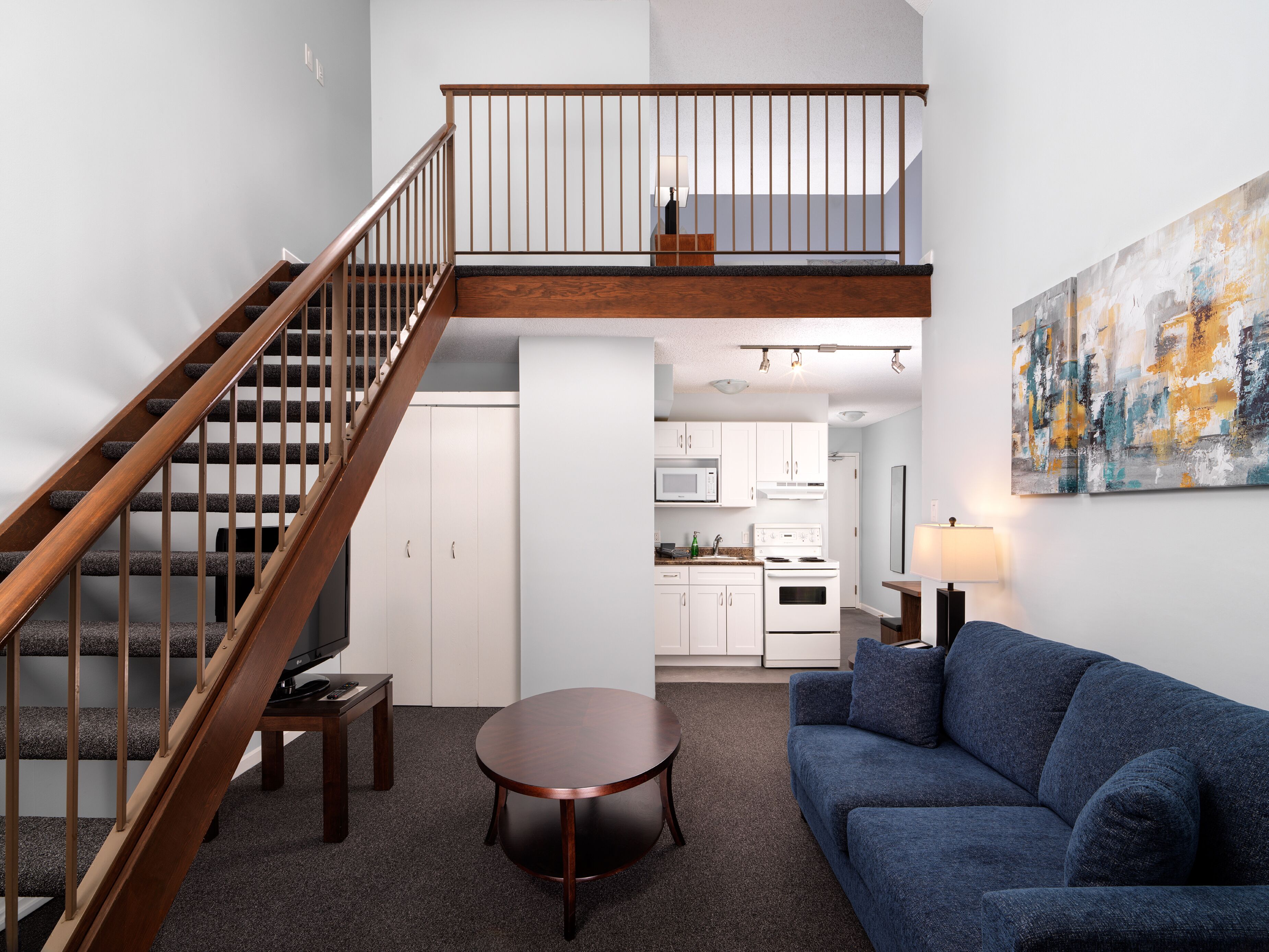Un espace de vie moderne avec un escalier en bois, un coin repas, un canapé et une cuisine en arrière-plan.