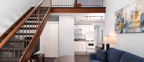A modern living space with a wooden staircase, a dining area, a sofa, and a kitchen in the background.