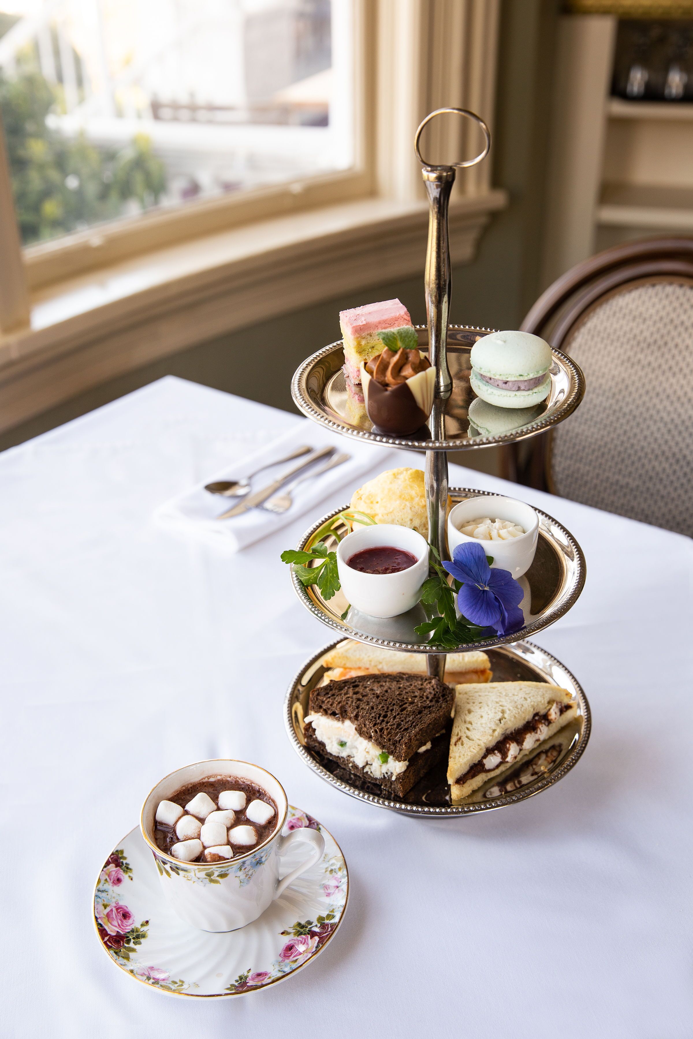 A tiered dessert stand with various sweets and a cup of hot chocolate on a table.