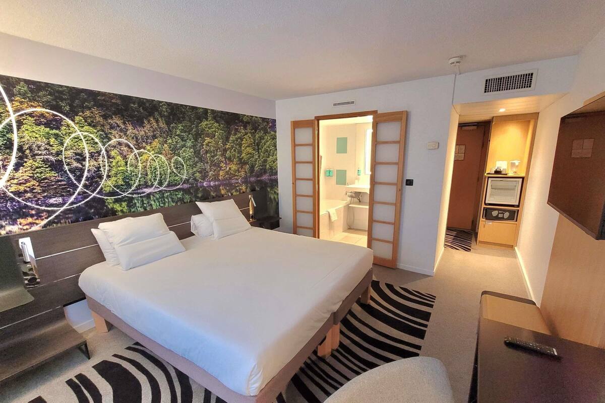 A hotel room with a bed, a desk, a chair, a bathroom, and a TV.
