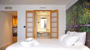 Ein Hotelzimmer mit einem großen Bett, einem Badezimmer mit Spiegel und einem Waldgemälde an der Wand.