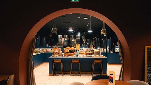 Ein Restaurant mit einer zentralen Insellinie, Barhocker und hängenden Pflanzen.