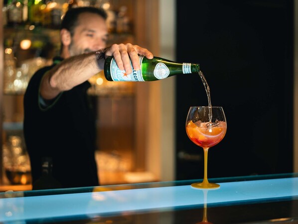 A person pouring a drink into a glass with a fruit garnish at a bar. - Novotel Lille Centre Grand Place (Lille)