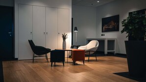 Ein moderner Arbeitsraum mit Holzboden, Schreibtisch, zwei Stühlen, einer Pflanzvase, einer Lampe und einem Bild an der Wand.