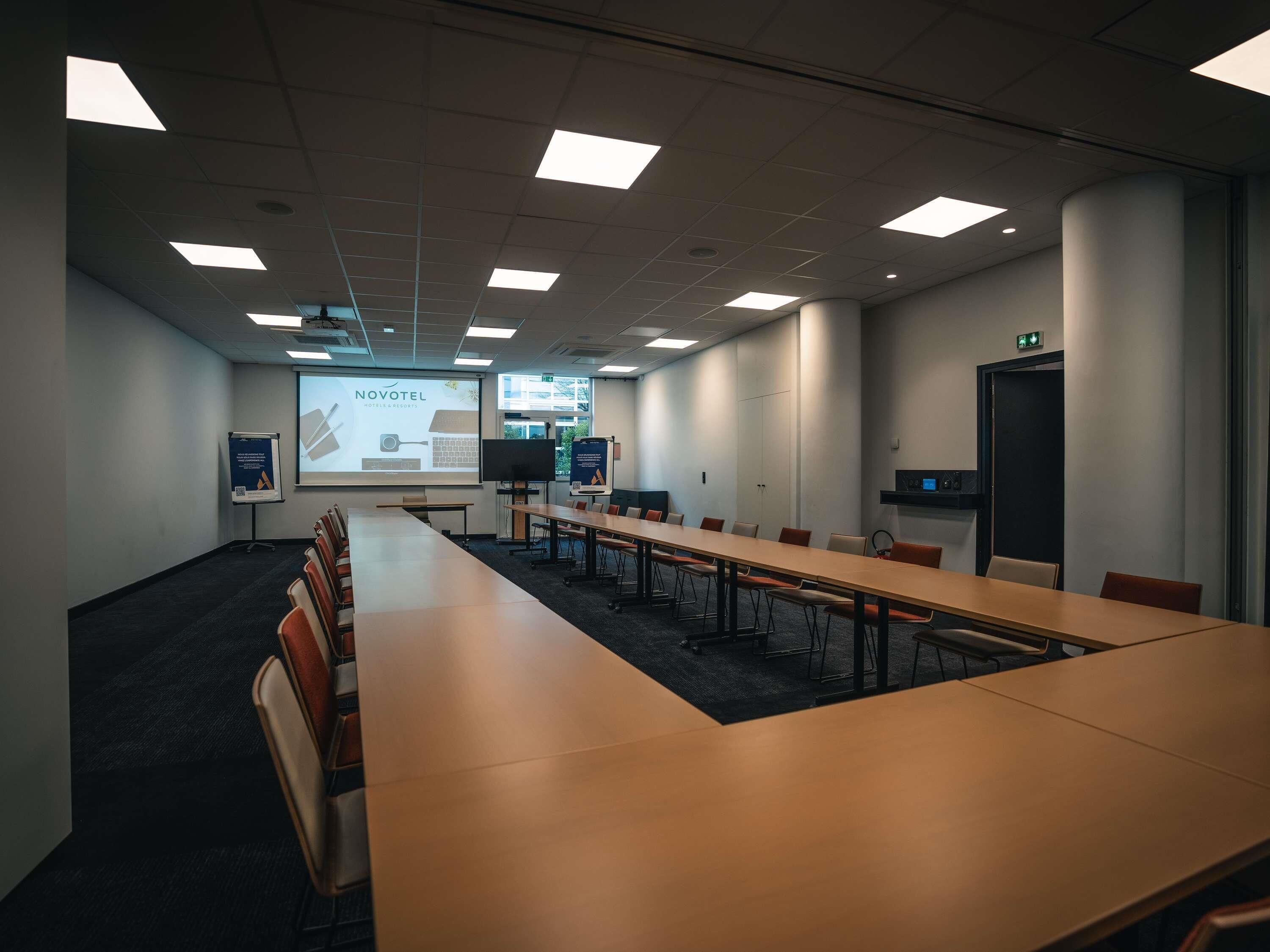 A conference room with a long table, chairs, a projector screen, and presentation boards.