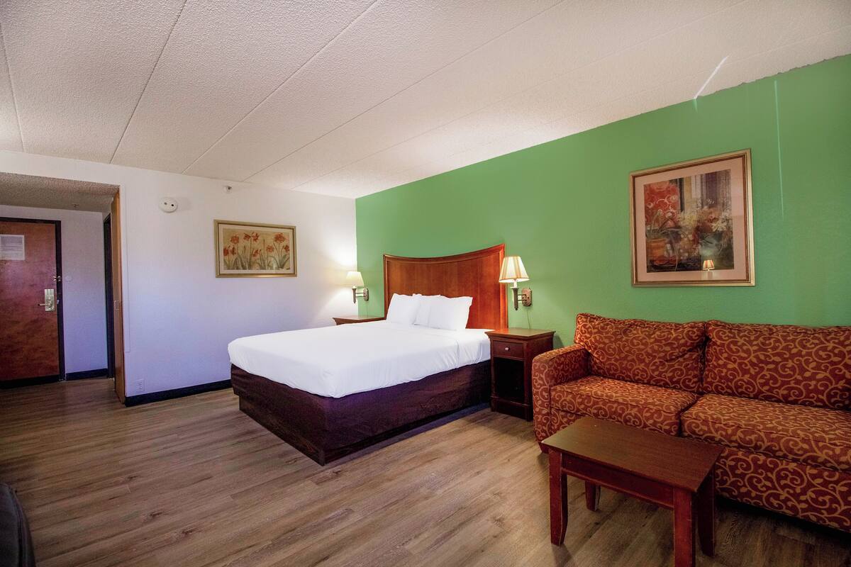 A hotel room with a bed, a sofa, a small table, and a painting on the wall.