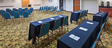 A conference room with rows of tables and chairs, a podium, and a carpeted floor.