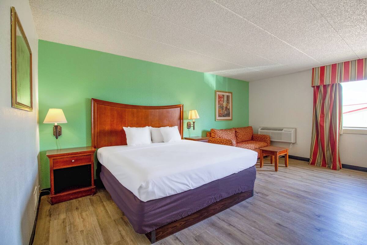 A hotel room with a large bed, a nightstand, a chair, a desk, and a window with curtains.