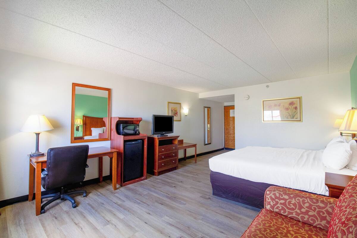 A hotel room with a bed, desk, chair, television, and dresser.