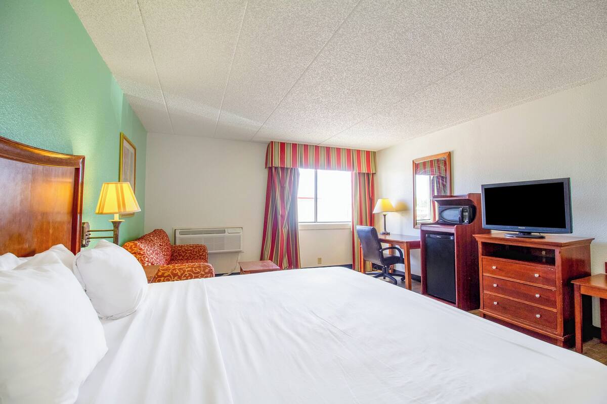 A hotel room with a large bed, a desk with a computer, a television, and a small refrigerator.