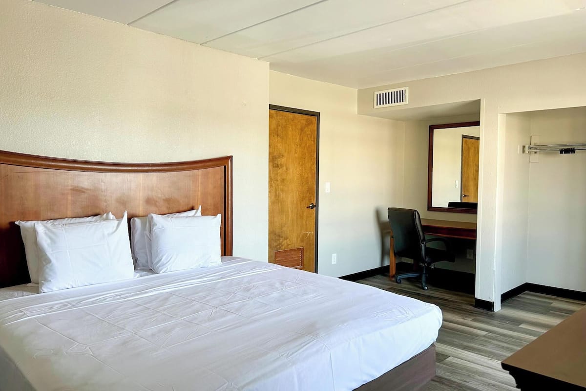 A hotel room with a large bed, a wooden headboard, a desk with a chair, and a mirror on the wall.