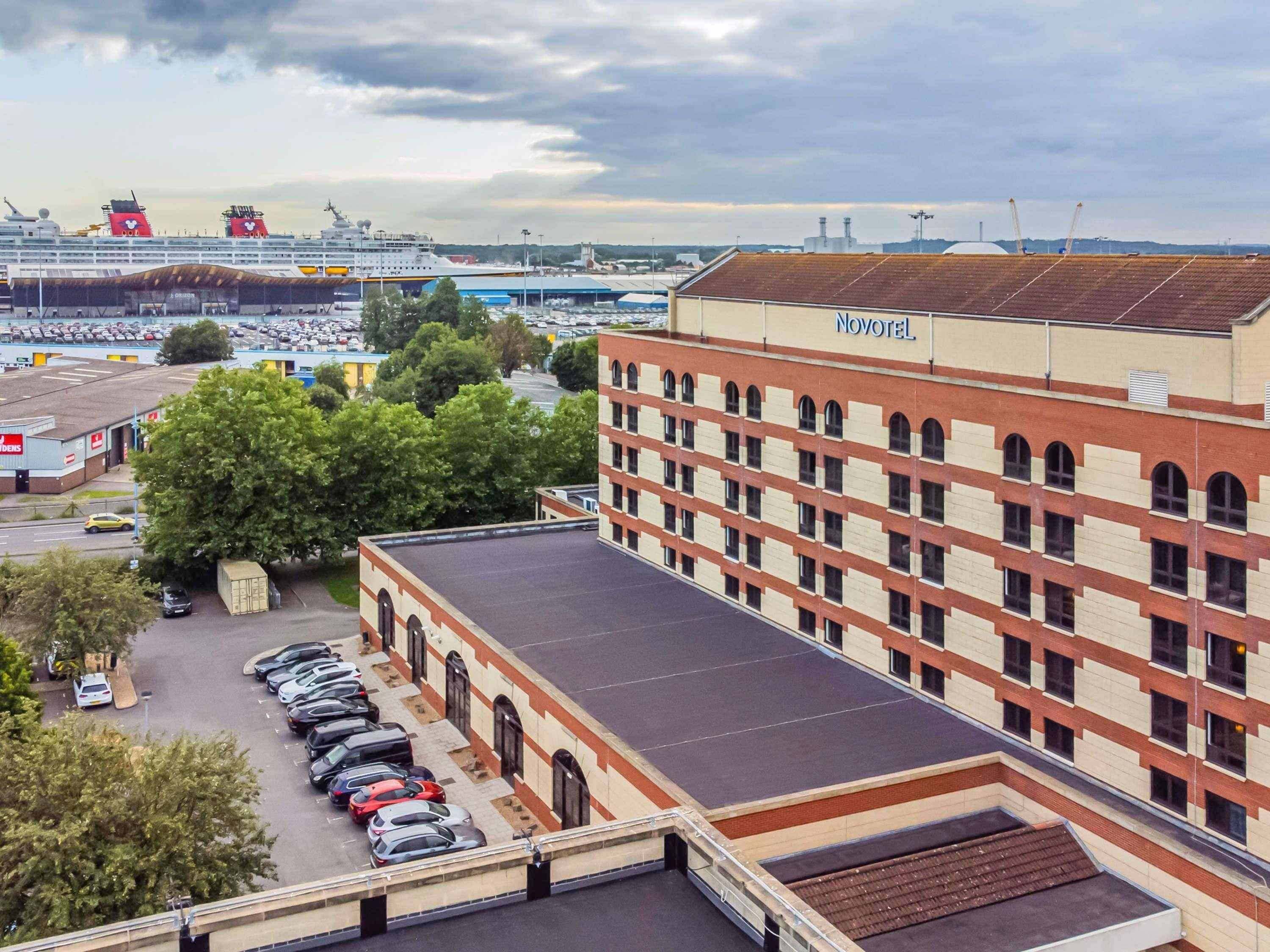 A hotel with a parking lot, a large building with a red and beige facade, and a cruise ship in the background.