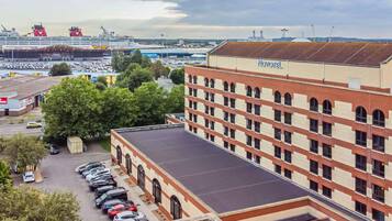 A hotel with a parking lot, a large building with a red and beige facade, and a cruise ship in the background.