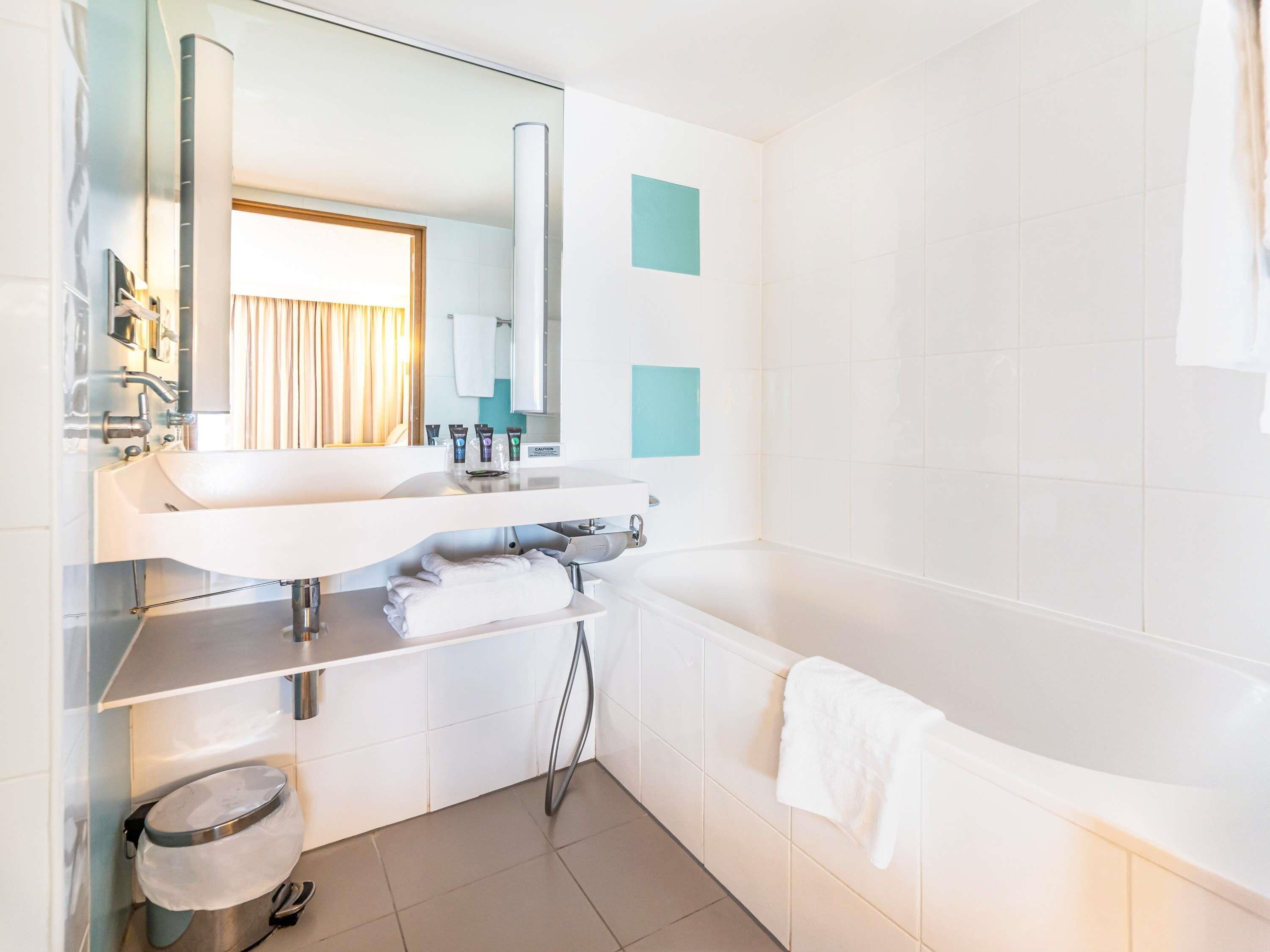 A modern bathroom with a white sink, mirror, and bathtub.