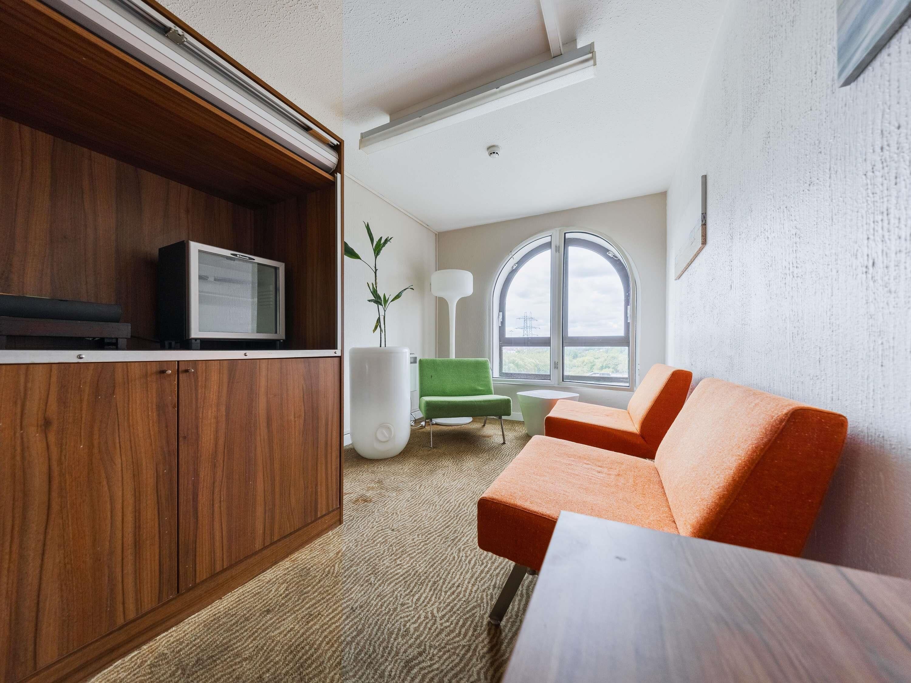 Ein modernes Wohnzimmer mit einem Holzkabinett, einem Fernseher, einem grünen Sessel, einem orangefarbenen Sofa und einem großen Fenster mit Blick.
