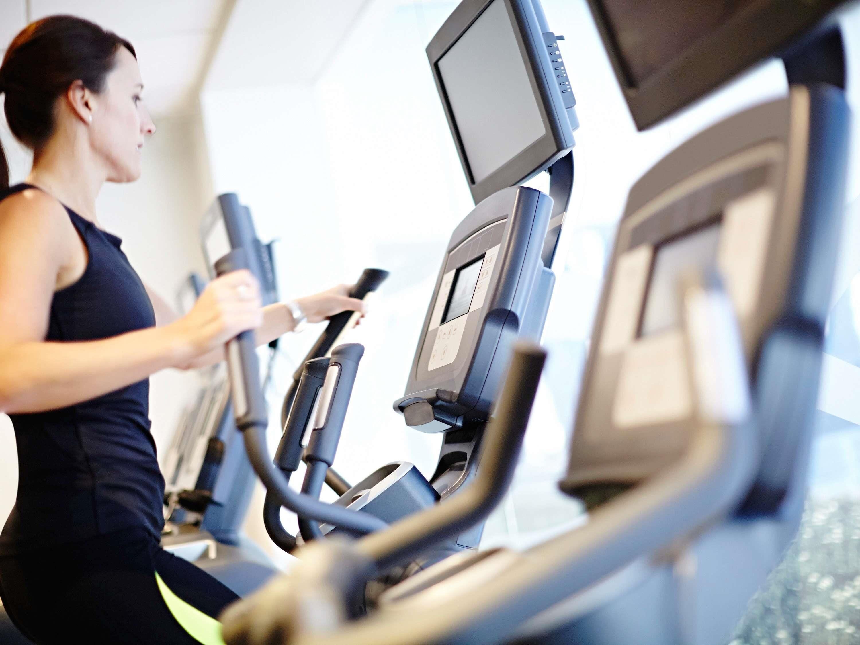 A woman using a stationary bike in a gym with a digital display.