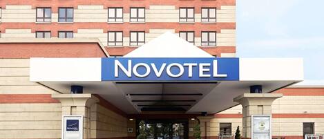 Der Eingang eines Novotel Hotels mit einer modernen Fassade, einer Überdachung und Blumentöpfen.