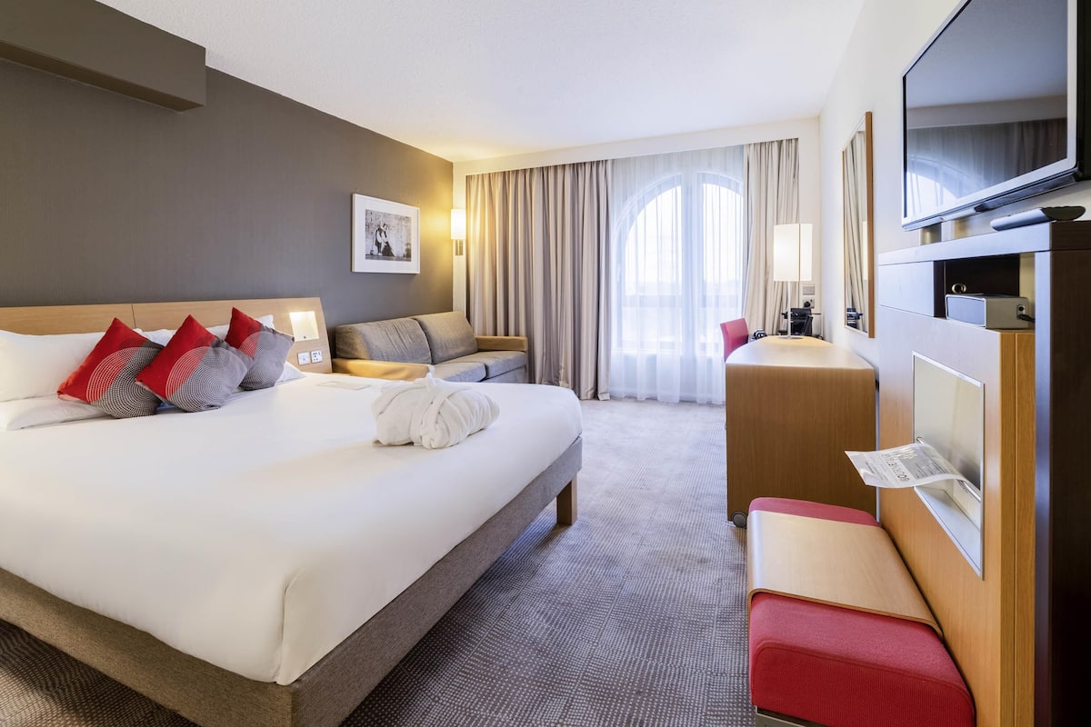 Een hotelkamer met een groot bed, een bureau, een televisie en een raam met gordijnen.