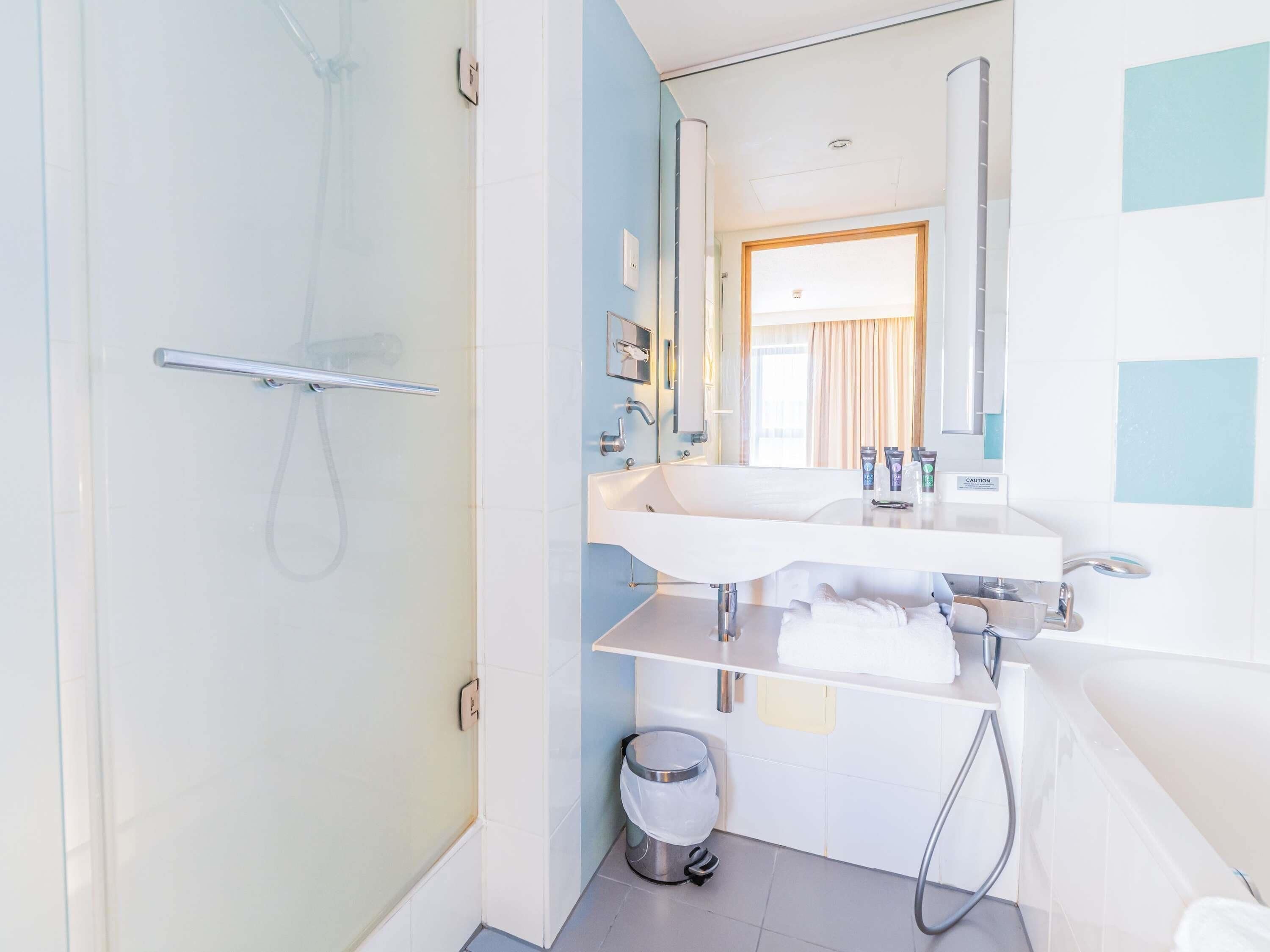Un baño moderno con cabina de ducha de vidrio, un lavamanos blanco con espejo y un perchero para toallas.