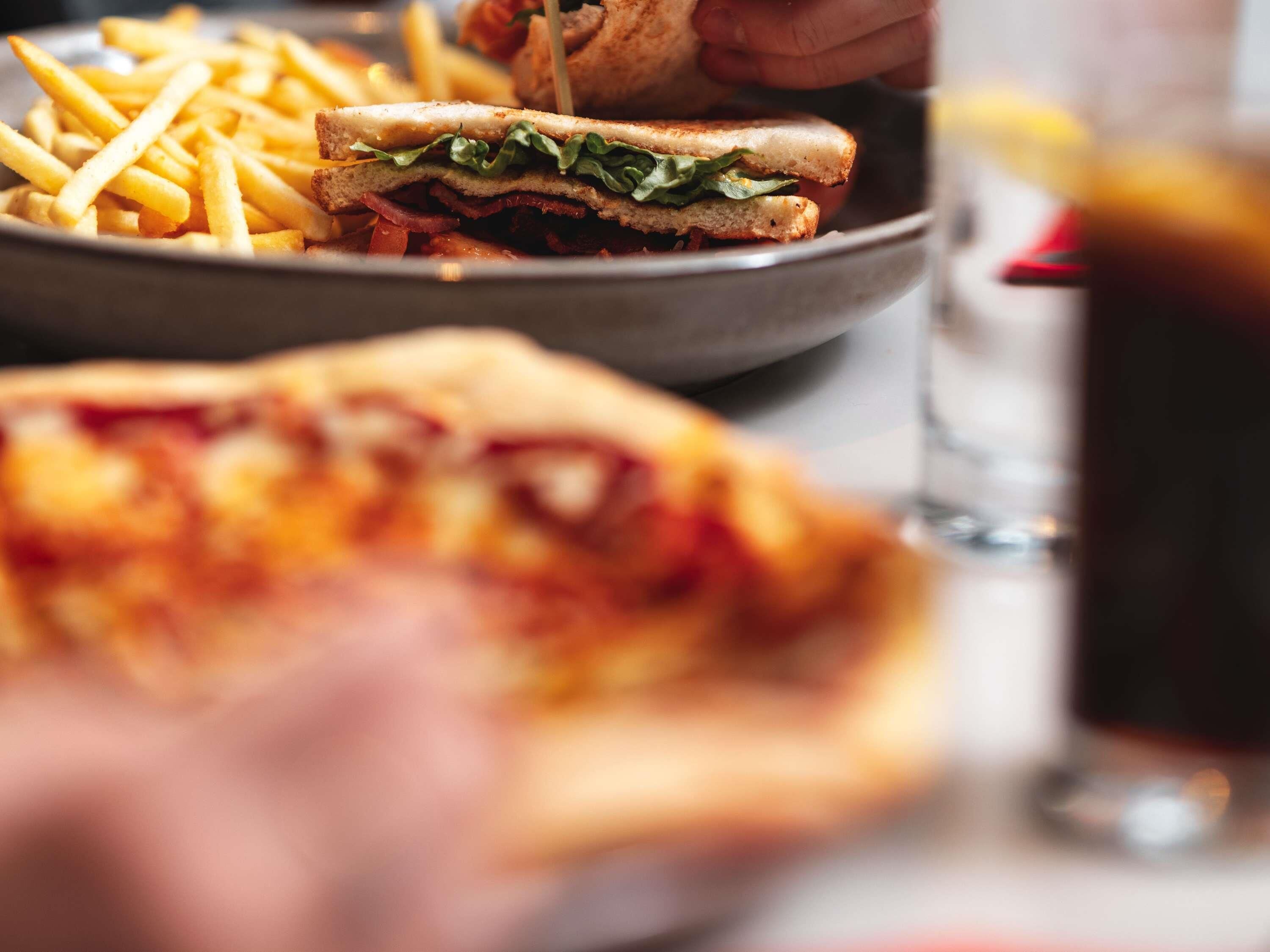 Een bord met frieten, een belegd broodje en een stuk pizza.