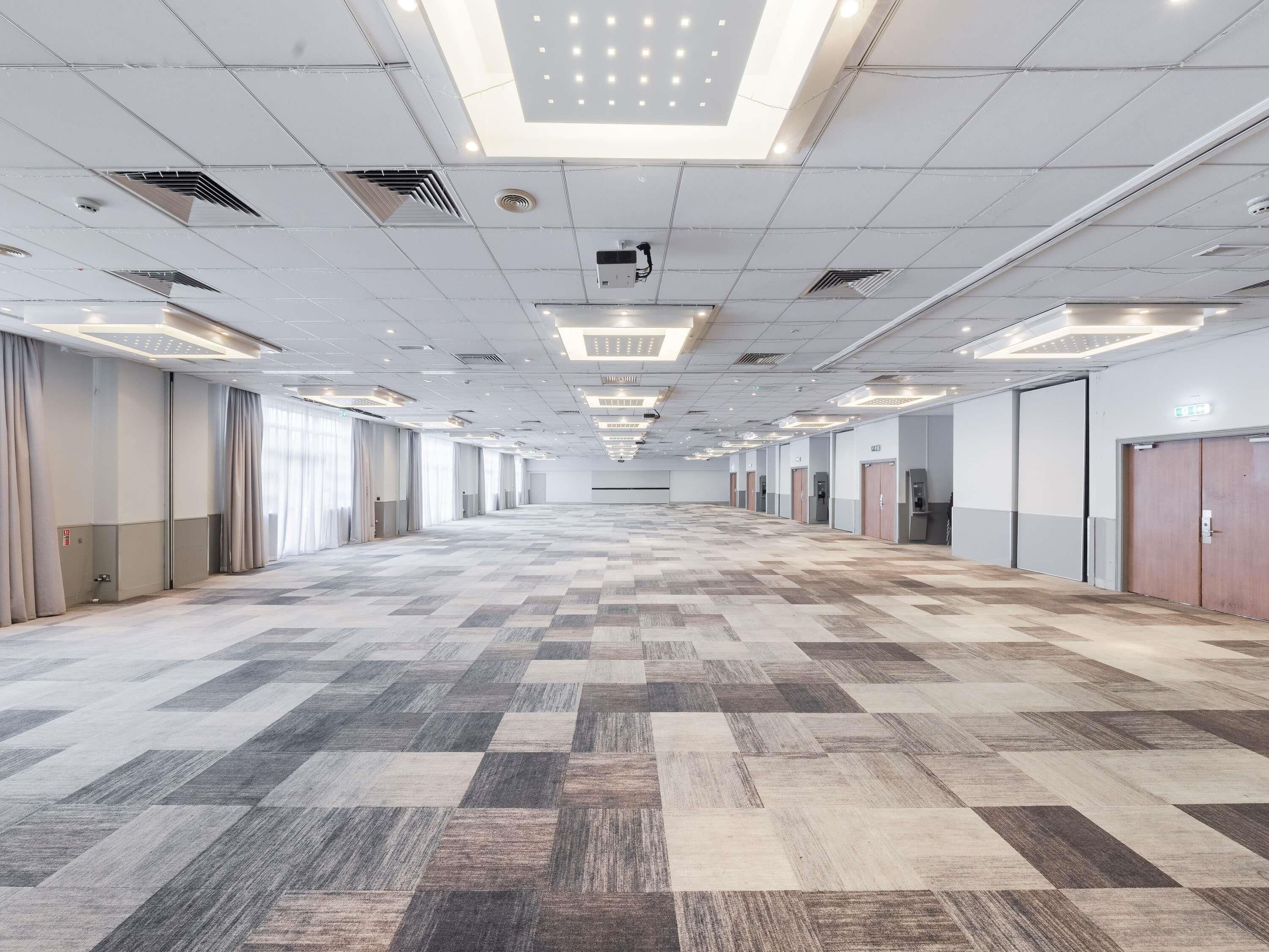 A spacious hotel interior with a checkered floor, ceiling lights, and doors along the walls.