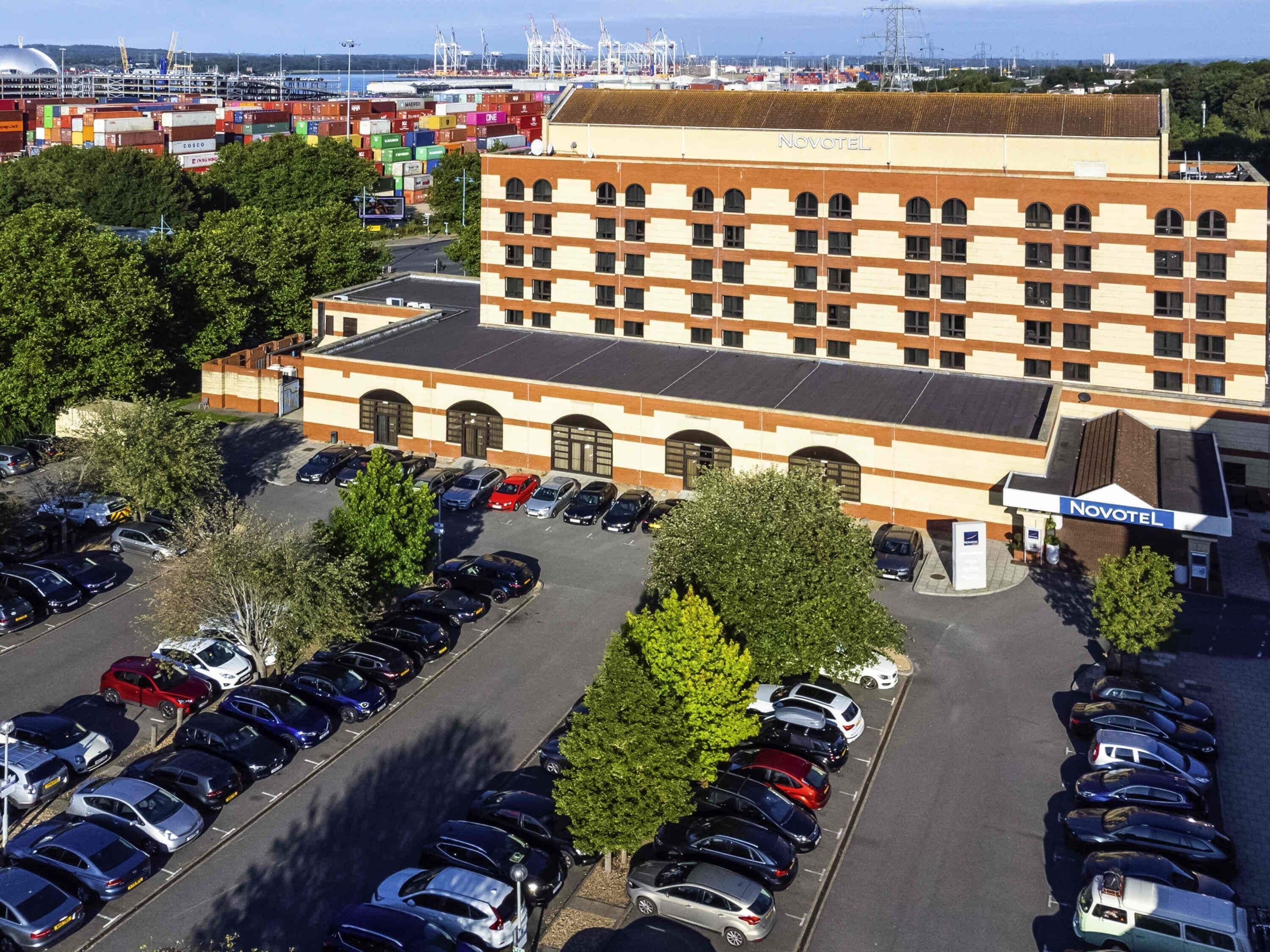 Hotel Novotel con parcheggio, diversi piani e vista su un porto con container.