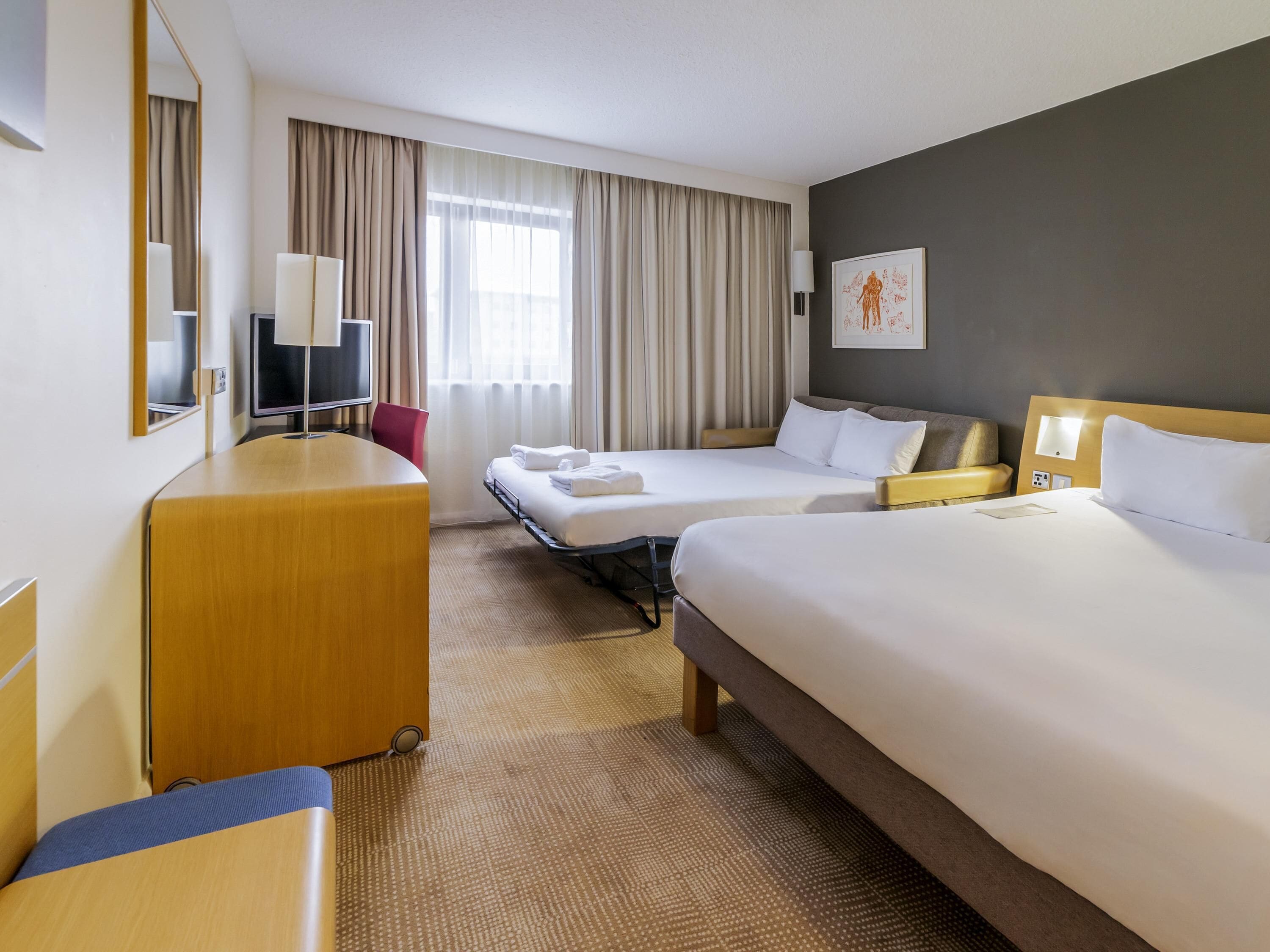 A hotel room with two beds, a desk, a chair, a TV, and a window with curtains.